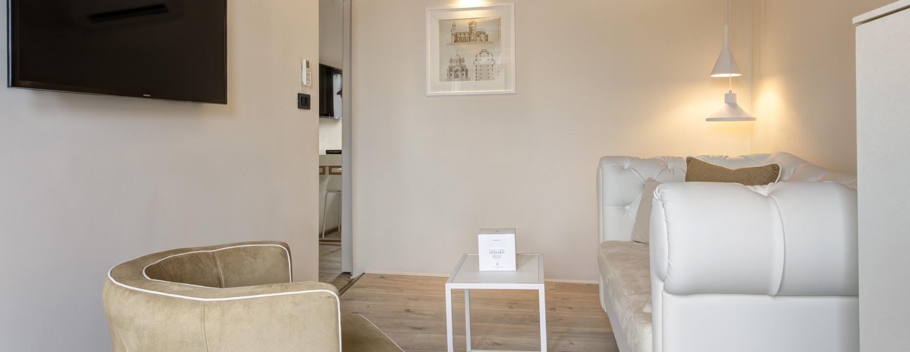 Camera d'hotel con poltrona marrone, divano bianco e TV.