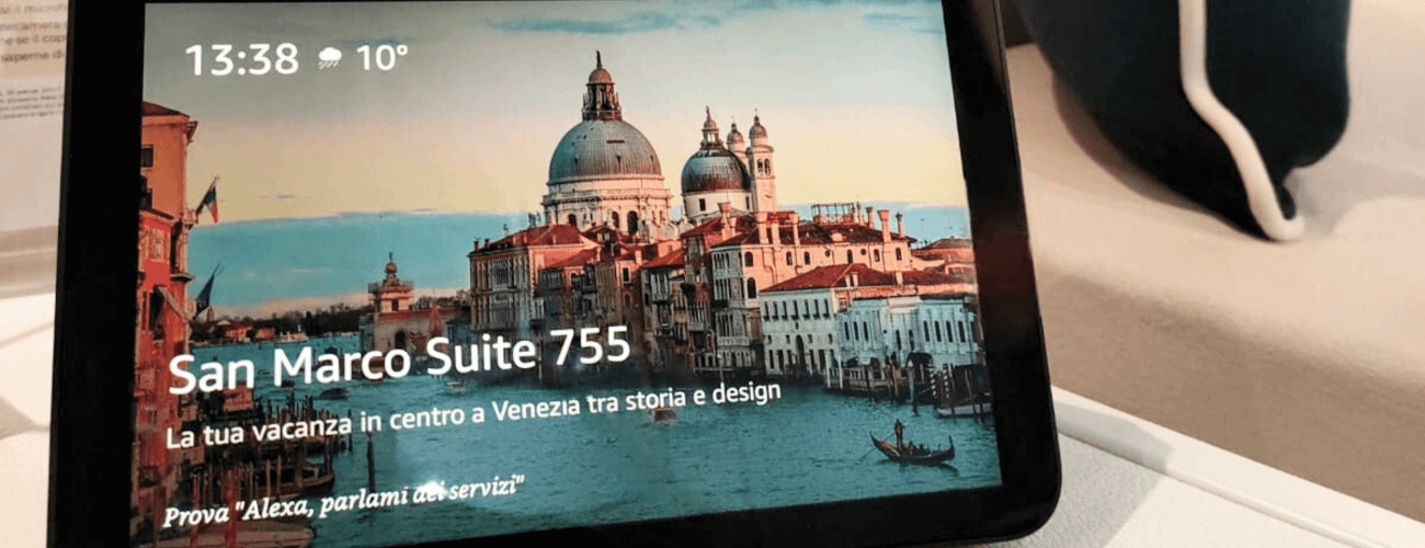 Tablet displaying a photo of Venice's Grand Canal, featuring a church, a boat, and weather info in a hotel room setting.