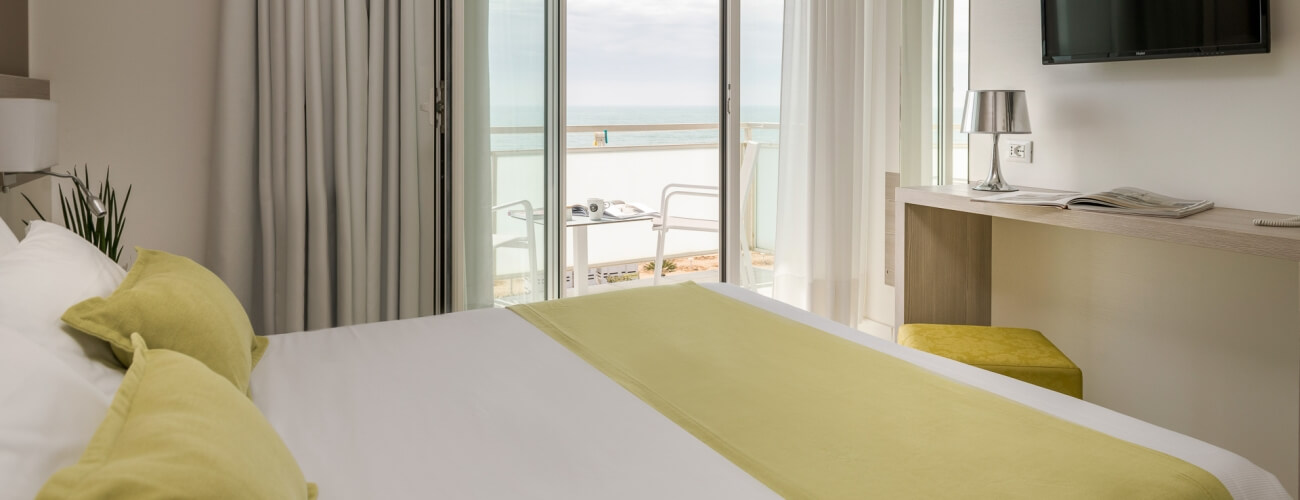 Ein ruhiges Hotelzimmer mit Blick auf den Ozean, geschmackvoll in Weiß und Limettengrün dekoriert, strahlt Gelassenheit aus.