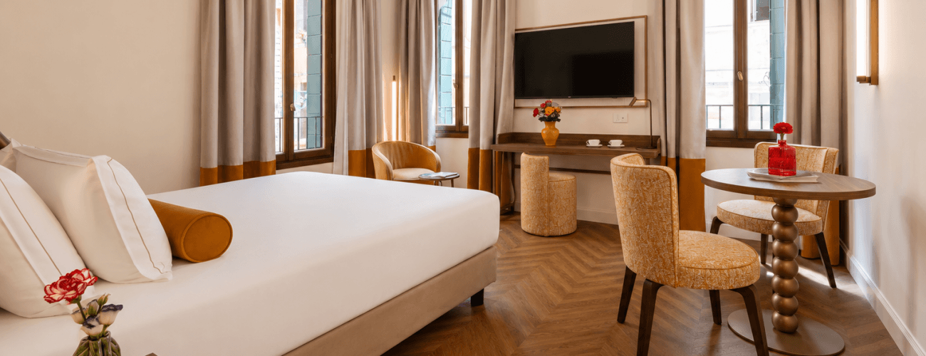 Camera d'hotel con letto, TV, scrivania e poltrone decorative.