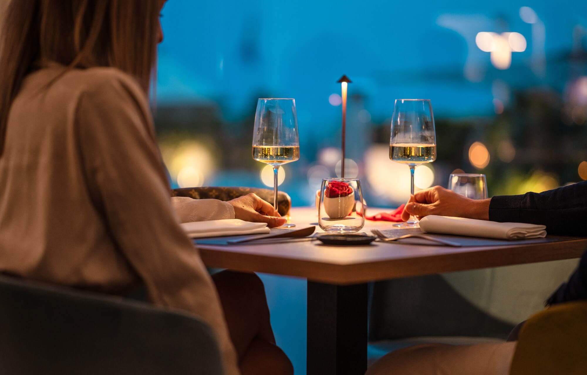 Una coppia seduta a un tavolo romantico con vino, rose e un'atmosfera accogliente in un ristorante.