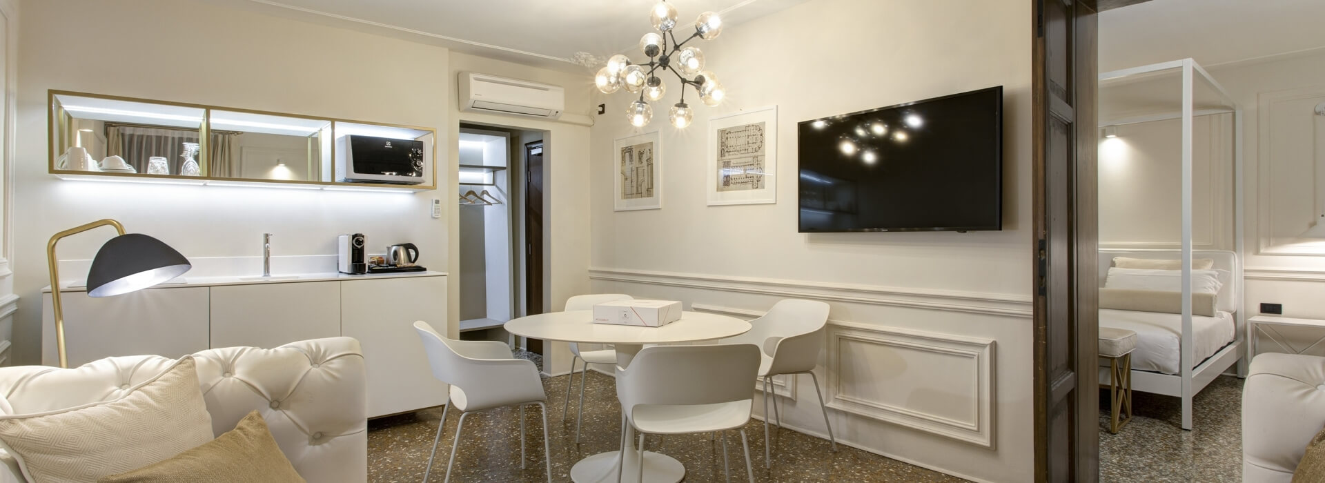 Camera d'albergo moderna e minimalista con divano bianco, cucina, tavolo da pranzo e letto con baldacchino. Atmosfera accogliente.