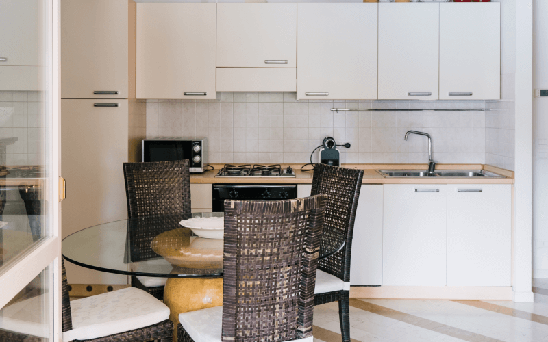 Moderne Küche mit weißen Schränken, Gasherd, Mikrowelle, Glastisch und Rattanstühlen auf gestreiftem Boden in Weiß und Braun.
