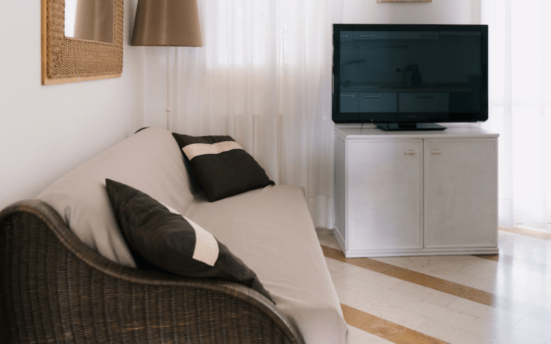 Wohnzimmer mit weißem Sofa, schwarzem Fernseher auf weißem Schrank und minimalistischer Gestaltung in neutralen Farben.