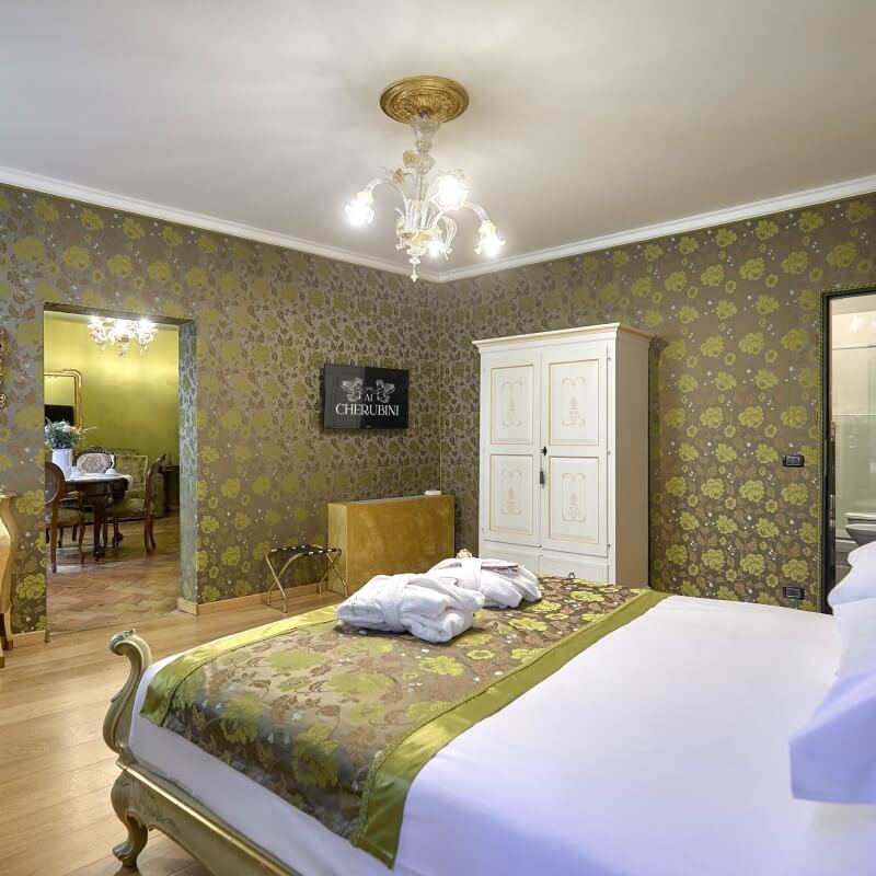 Camera d'hotel con letto, armadio, TV e area pranzo.