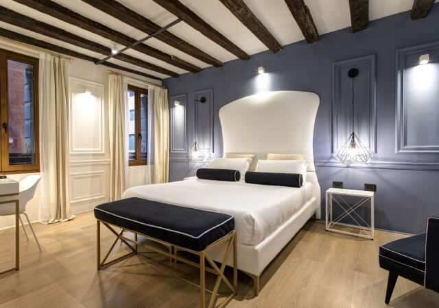 Camera d'albergo con letto king-size, pareti blu e dettagli bianchi.