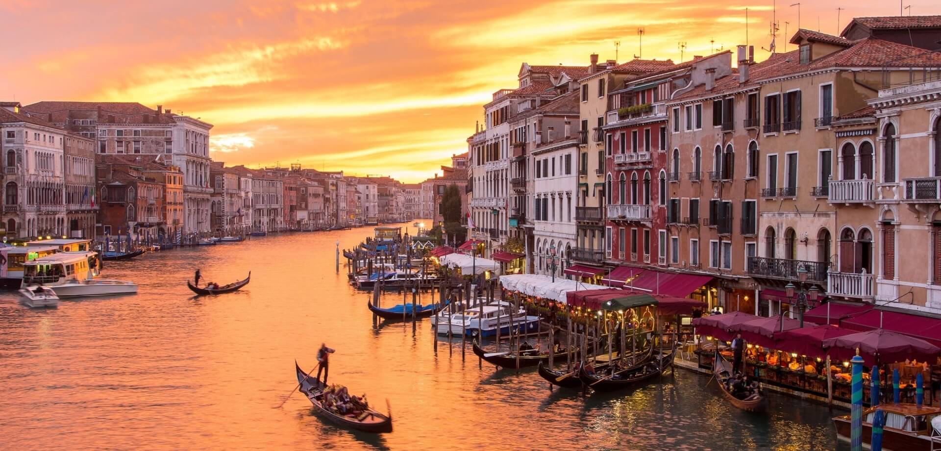 Una scena di Venezia al tramonto, con canali, gondole e edifici storici illuminati da colori caldi.