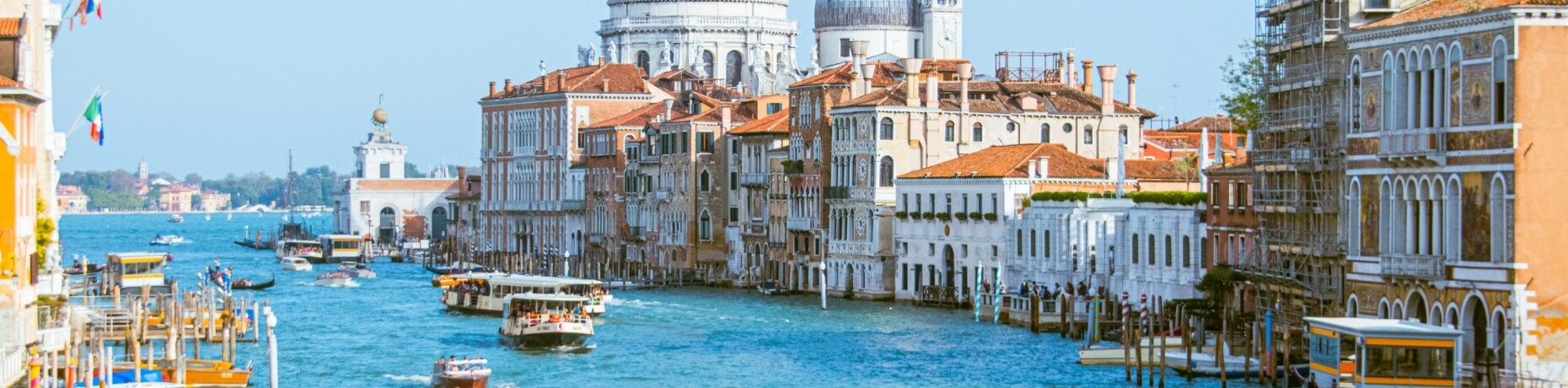 Una vivace scena del Canal Grande a Venezia, con barche, edifici colorati e la chiesa di Santa Maria della Salute sullo sfondo.
