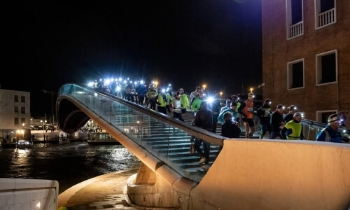 Gruppo di persone sale scale su un ponte moderno illuminato.