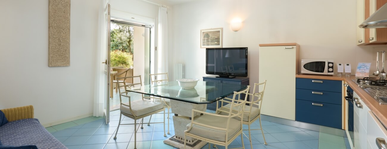 Moderne Küche und Essbereich in Blau und Weiß mit Marmortisch, blauer Couch und offener Terrassentür.