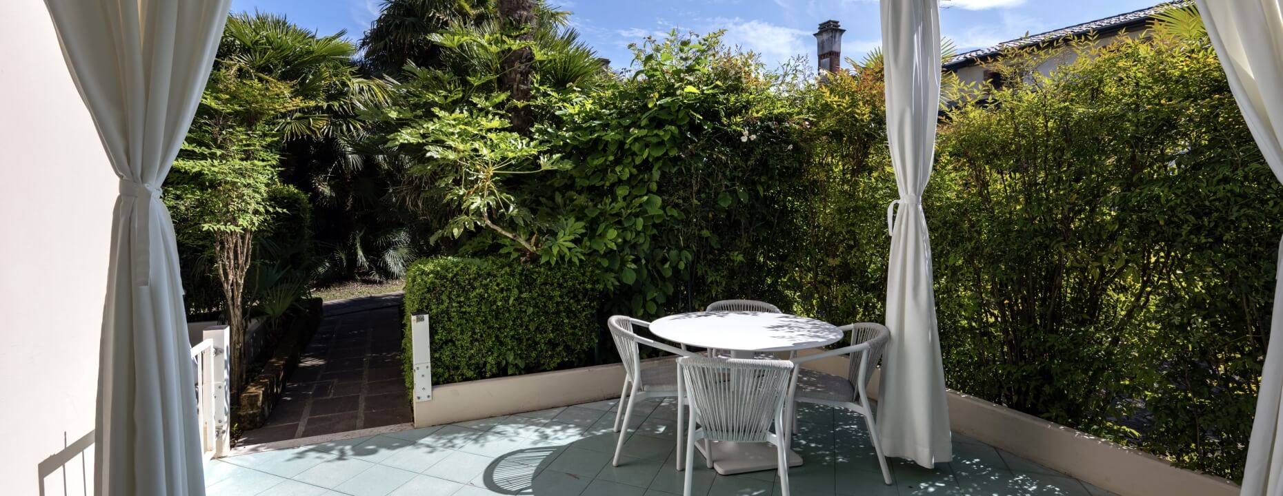 Tavolo bianco rotondo con quattro sedie bianche, sfondo verde.