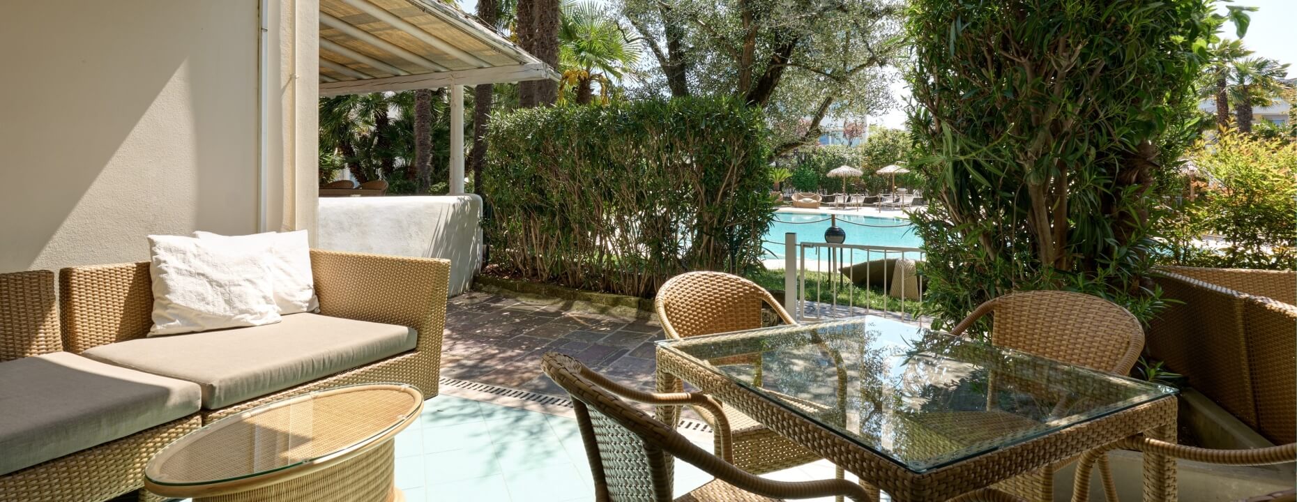 Area esterna con divano, tavolo e piscina blu sullo sfondo.