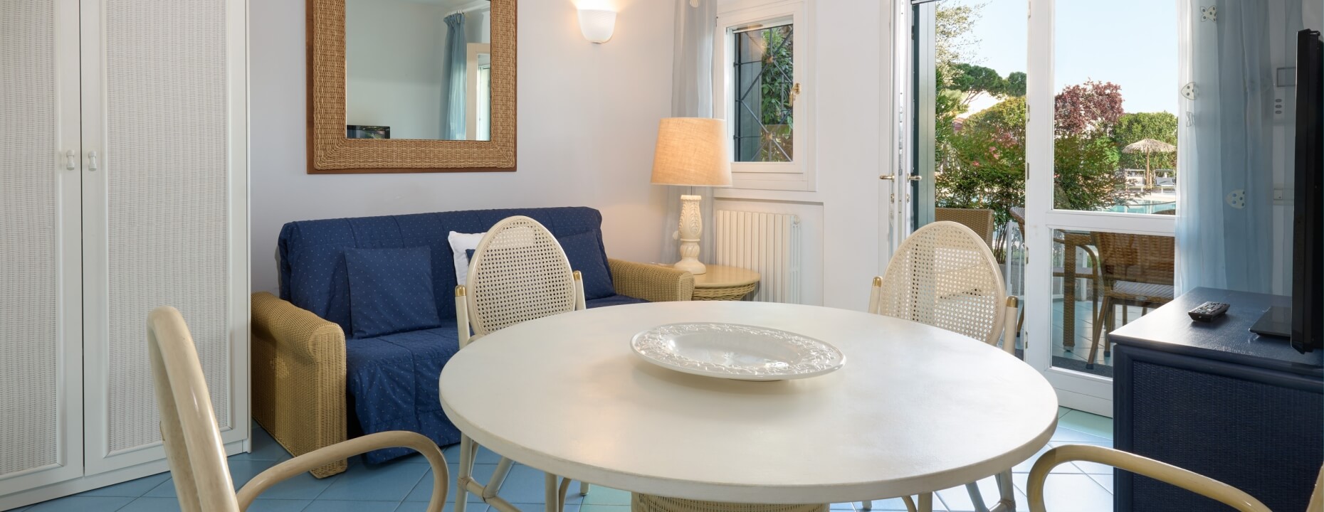 Soggiorno con divano blu, tavolo bianco e vista su piscina.