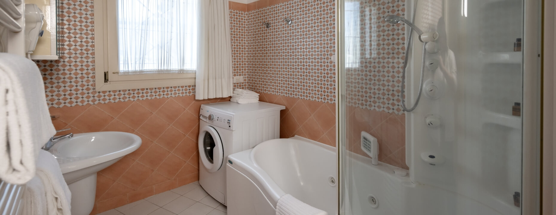 Bagno con lavabo, lavatrice, vasca, doccia e pareti piastrellate.