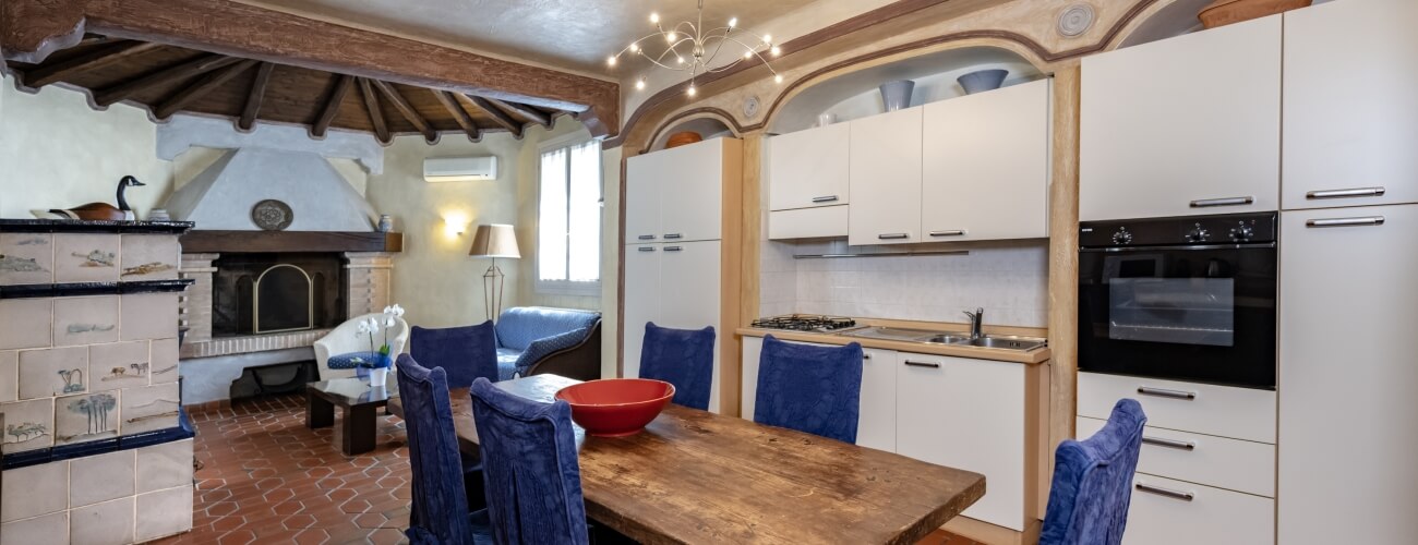 Cozy living room and kitchen with white cabinets, blue-upholstered chairs, fireplace, and inviting decor.