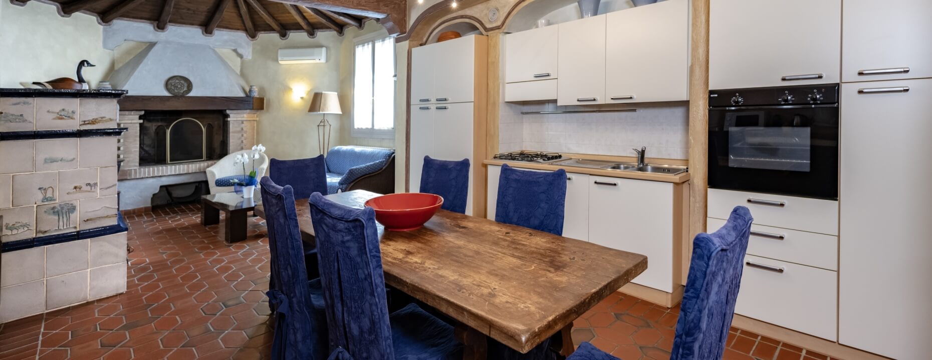 Area pranzo e cucina con tavolo, camino e divano blu.