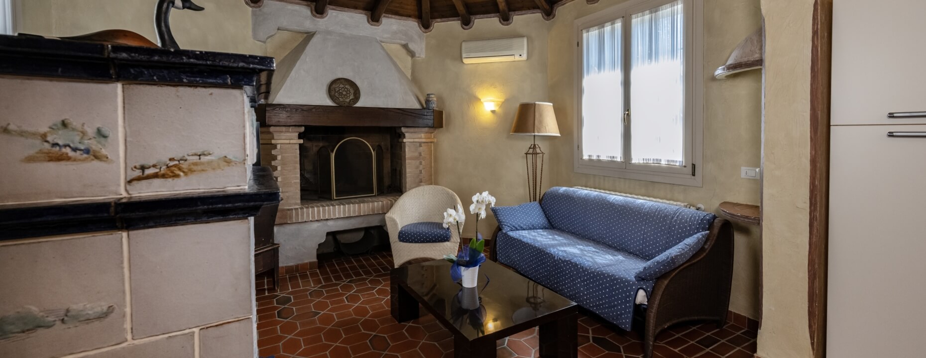 Area salotto con divano, poltrona, camino e lampada da terra.