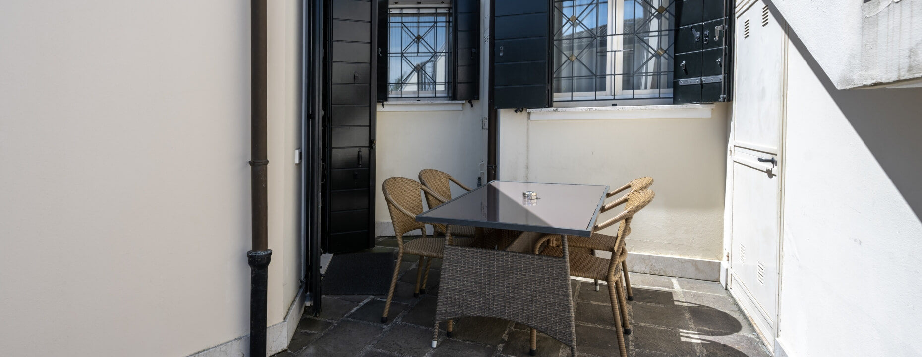 Area esterna con tavolo grigio, sedie in vimini e finestre.