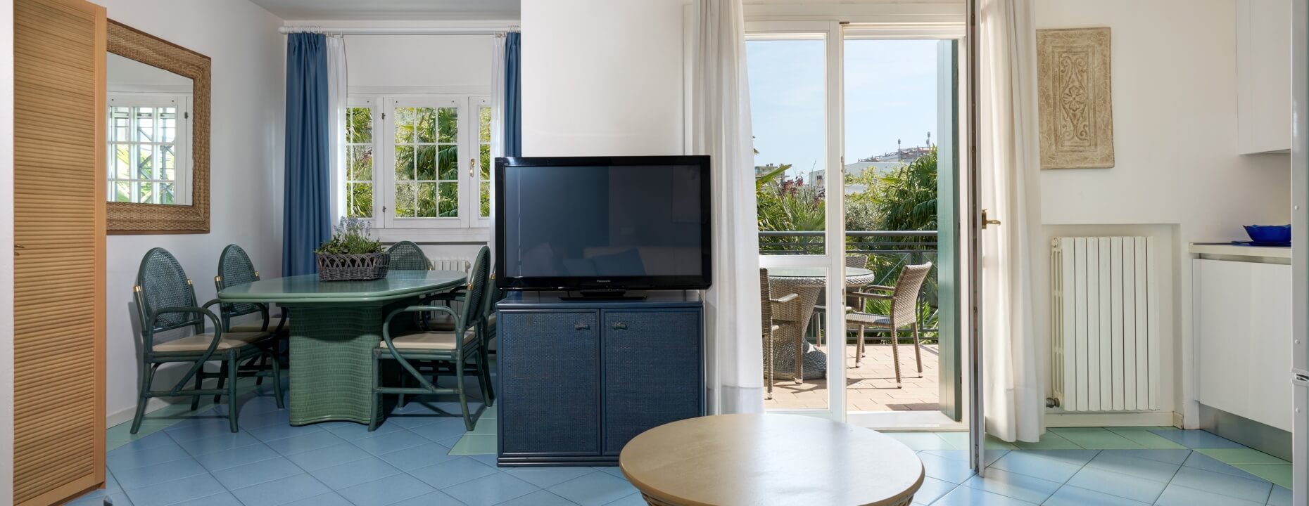 Soggiorno con tavolo da pranzo, TV e porta scorrevole per balcone.