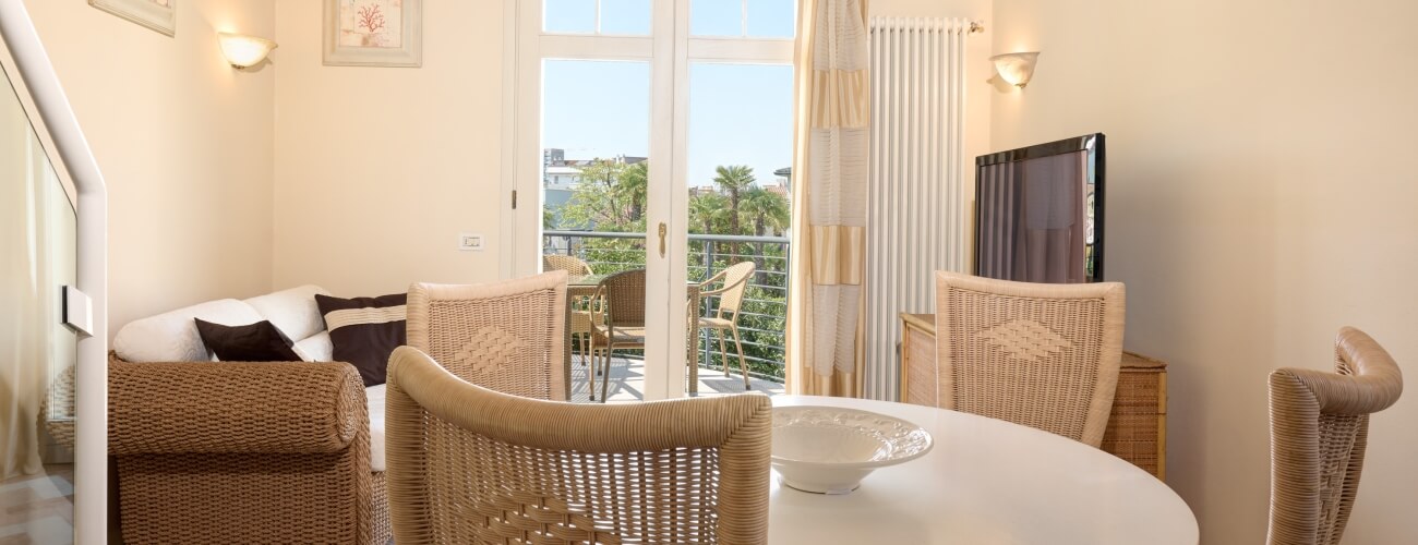 Serene beachside living space with wicker furniture, white table, balcony view, and light-striped curtains.