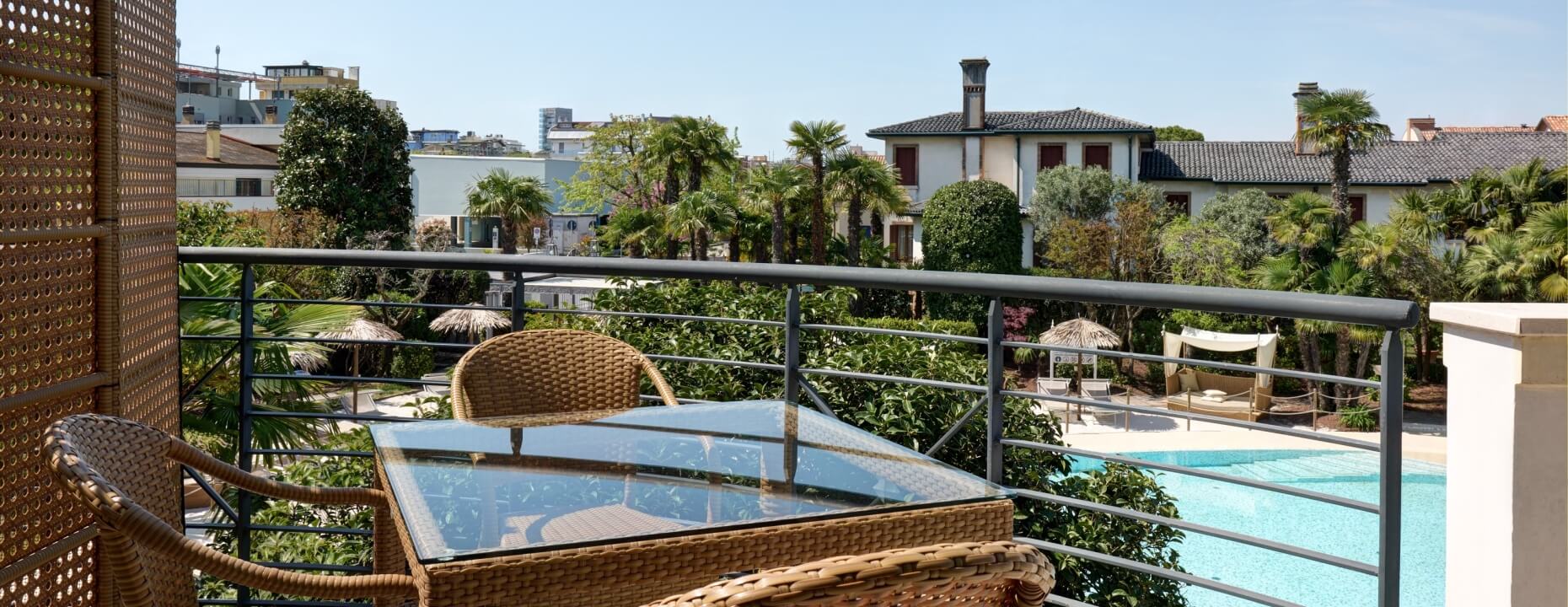 Balcone con tavolo e sedie, vista su piscina e verde.