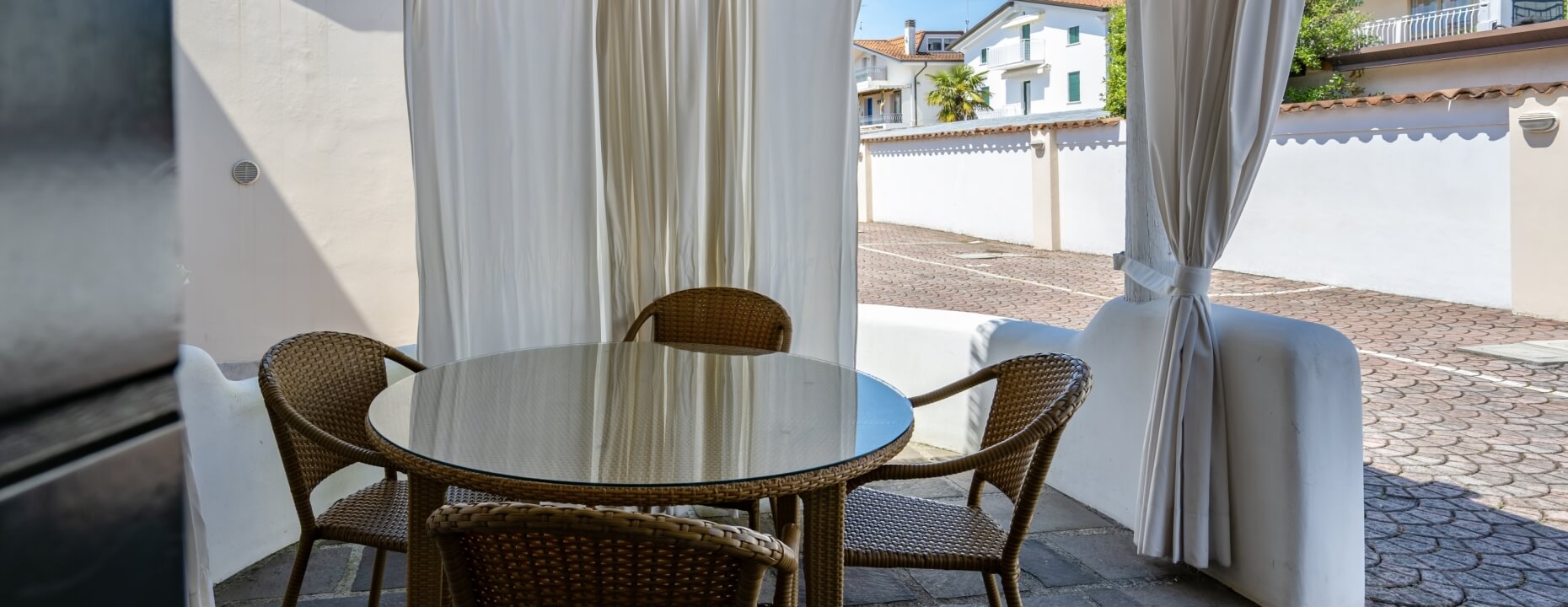 Tavolo rotondo in vetro con sedie in vimini su patio.