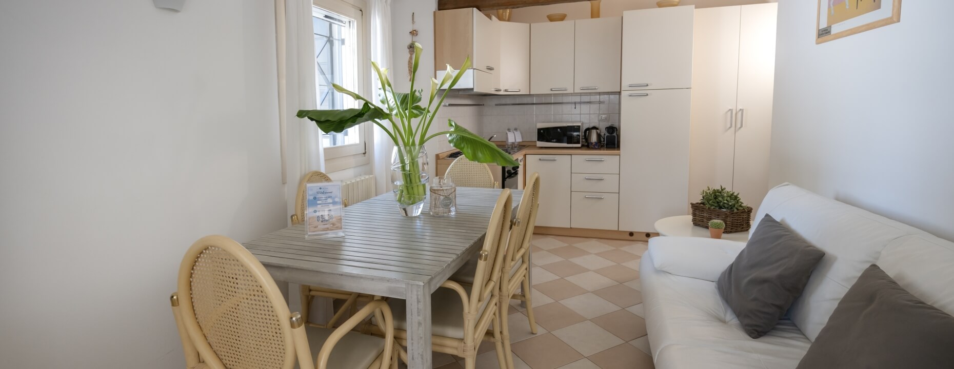 Studio apartment with dining table, sofa, kitchenette, and window.   Appartamento studio con tavolo da pranzo, divano, angolo cottura e finestra.