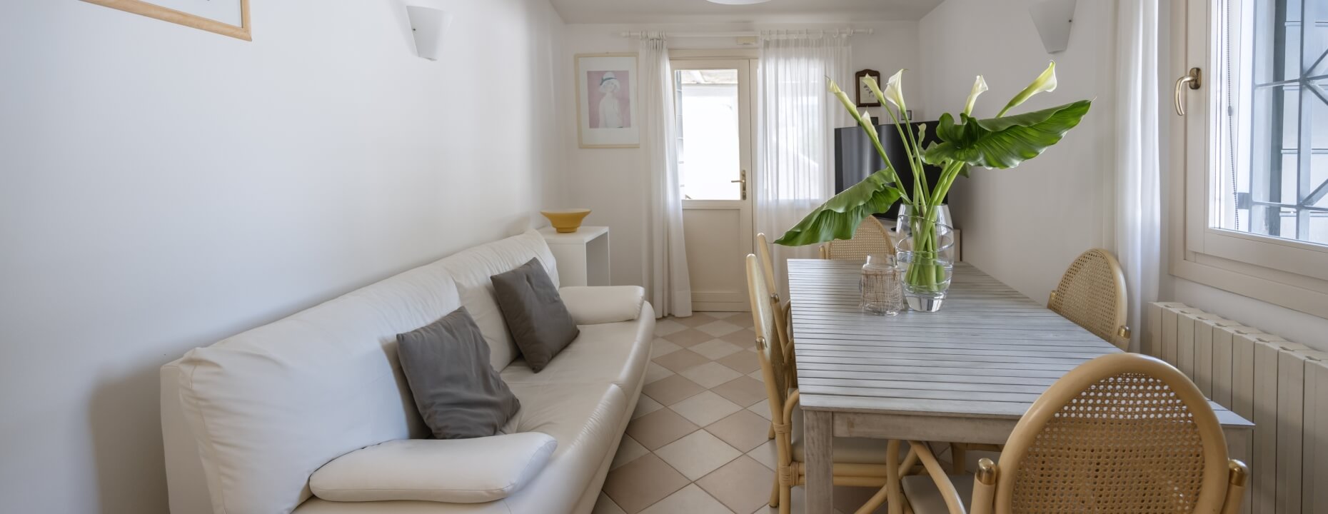 Soggiorno con divano bianco, tavolo in legno e fiori bianchi.