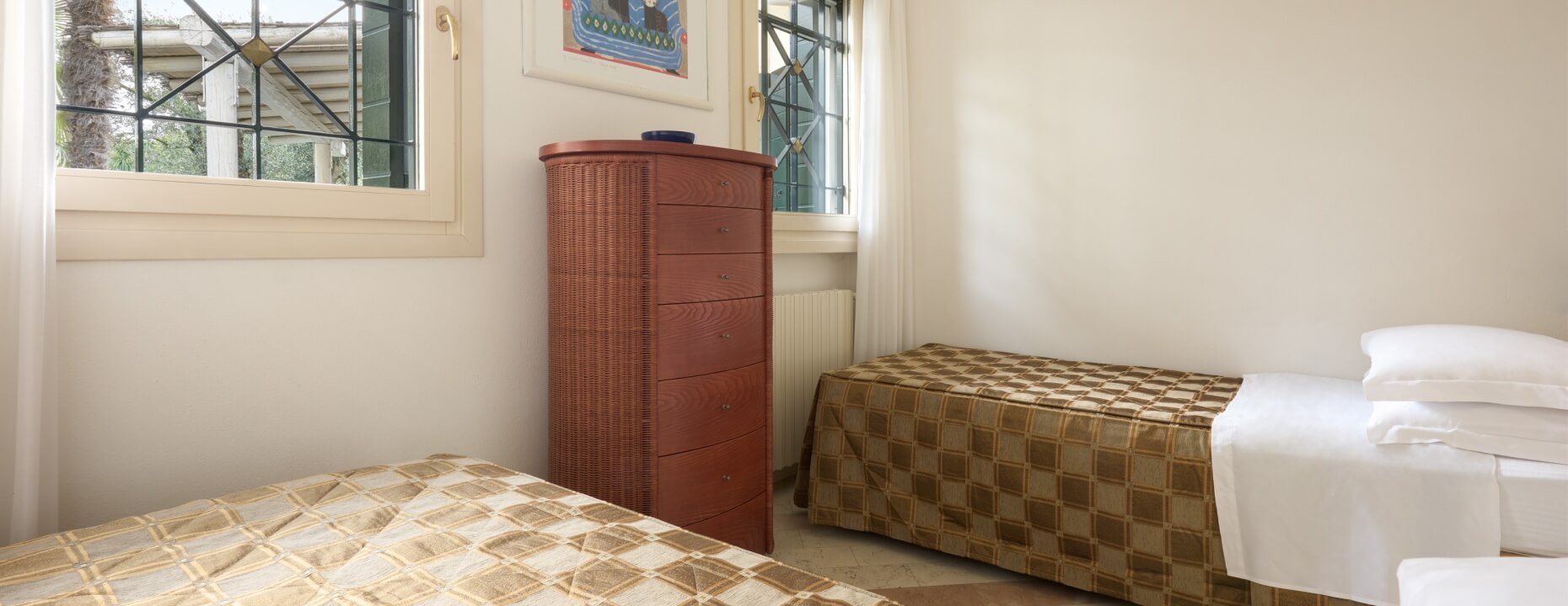 Camera d'hotel con due letti, cassettiere e finestre decorate.