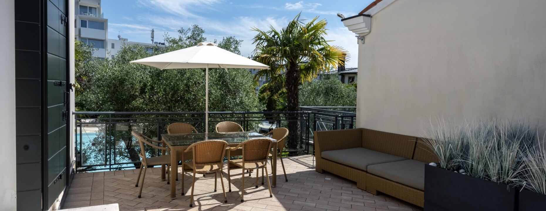 Area esterna con tavolo, sedie, divano e piscina sullo sfondo.