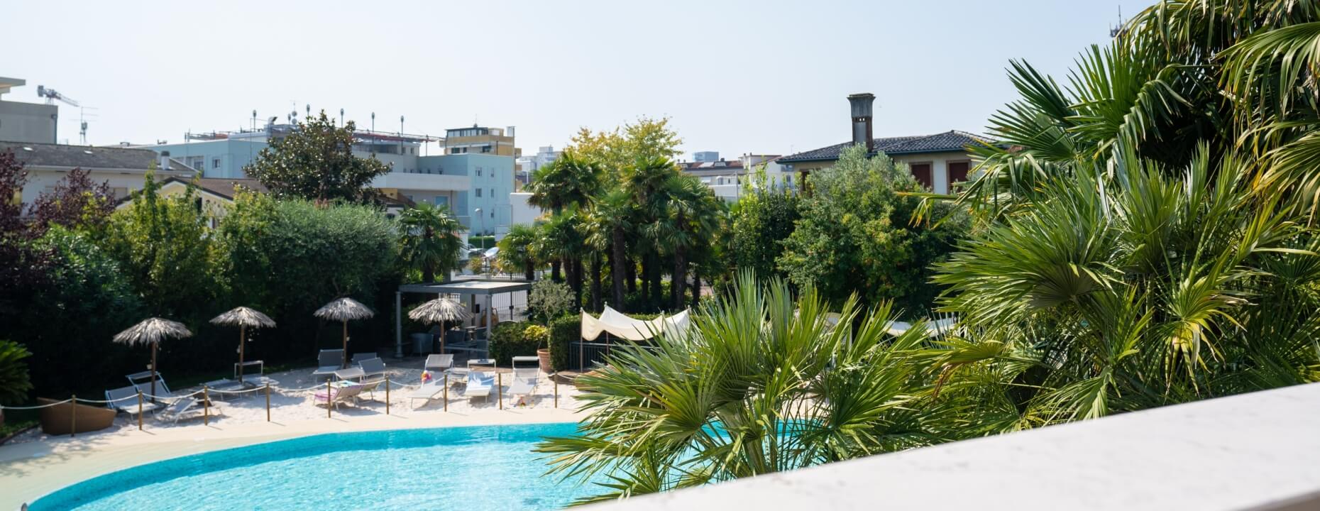 Piscina blu curvilinea con lettini e ombrelloni, circondata da alberi.