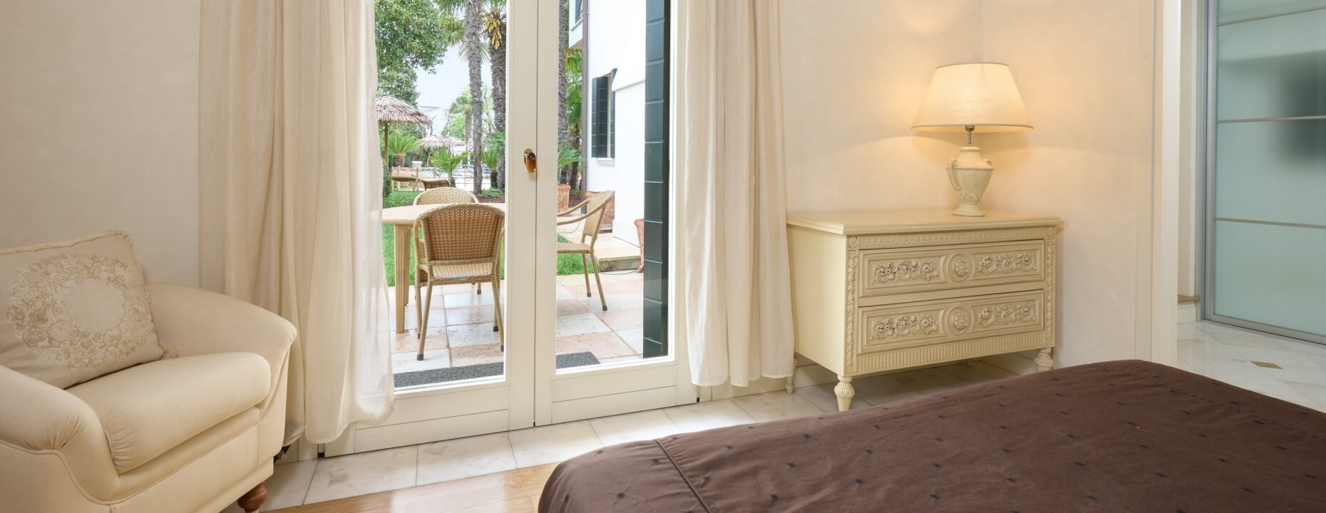 Camera d'hotel con letto, armadio, poltrona e porte francesi.