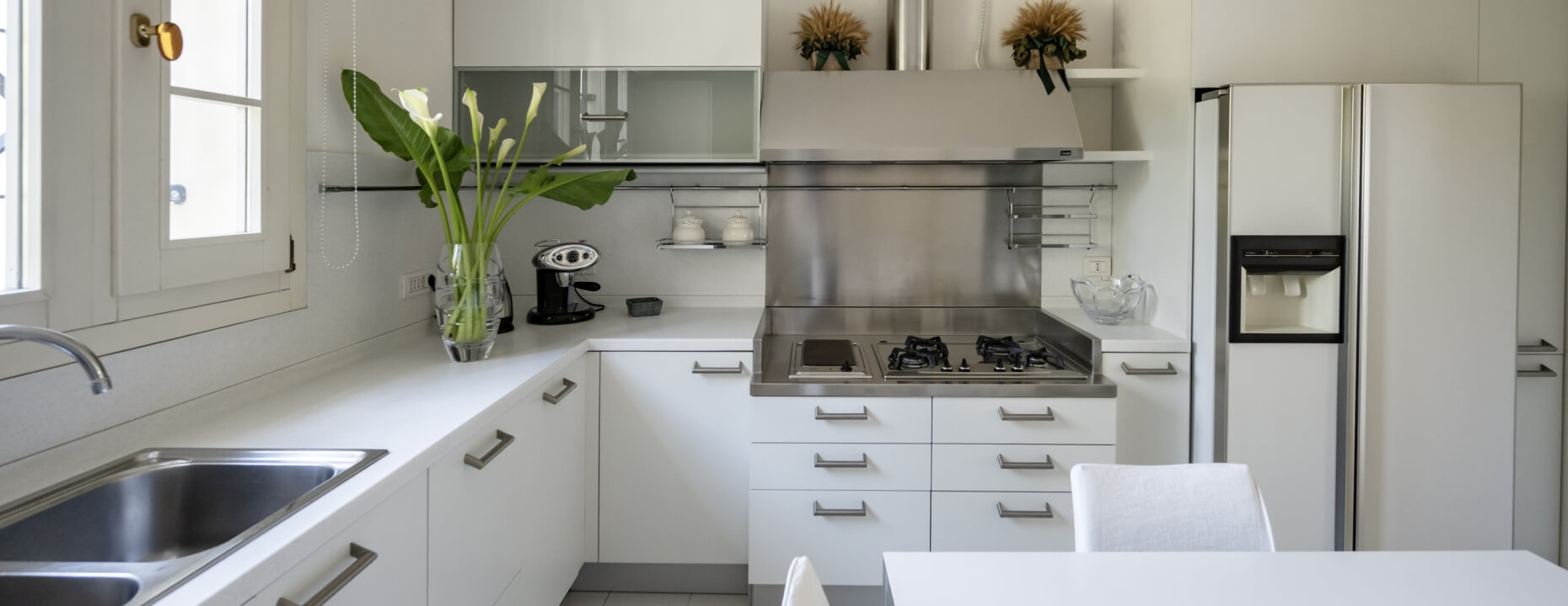 Cucina moderna bianca con lavello, fiori e macchina da caffè.