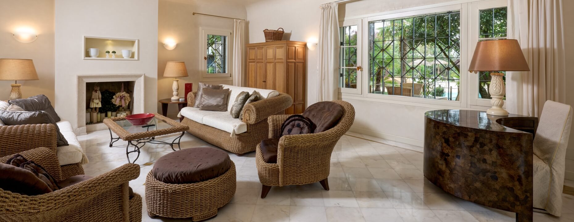 Soggiorno con mobili in rattan, camino e grandi finestre.