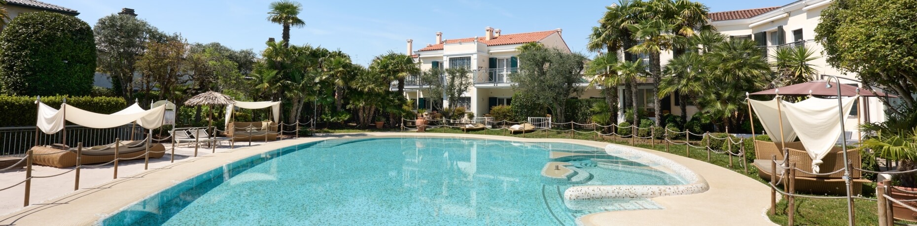 Scène de piscine sereine avec des chaises longues, entourée de verdure luxuriante et d'un ciel bleu clair.