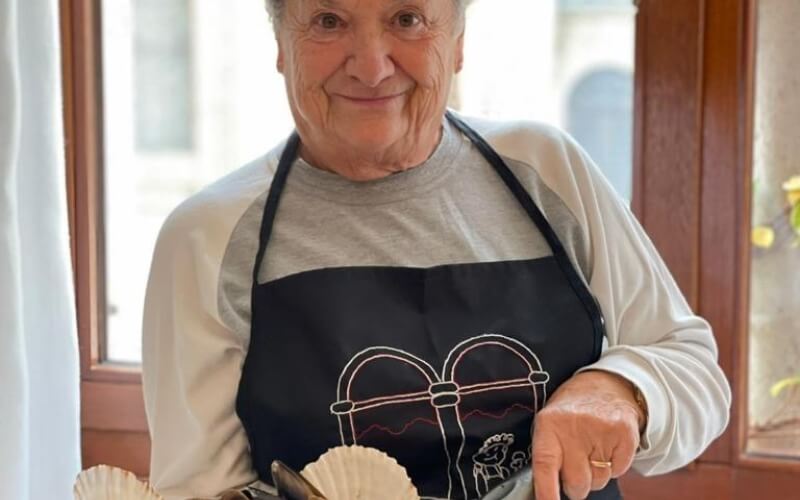 Donna anziana con grembiule nero tiene un piatto di capesante.