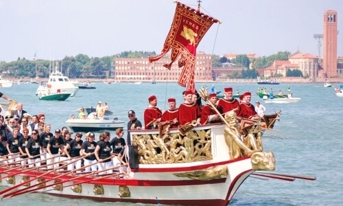 Barca decorata con figure dorate e persone in tuniche rosse a Venezia.