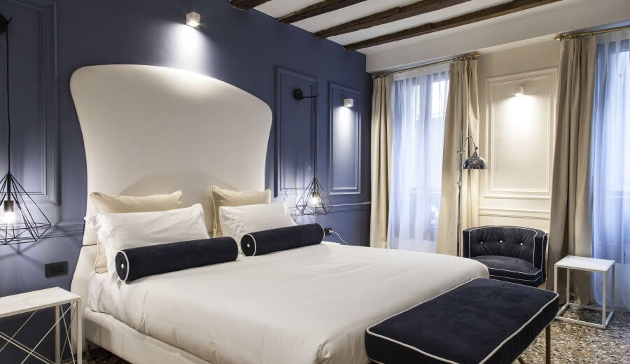 Camera d'hotel con letto bianco, poltrona blu e decorazioni geometriche.