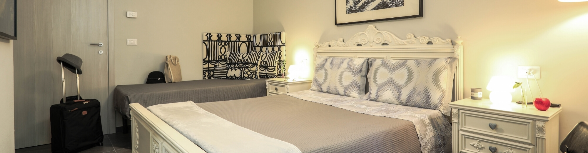 Camera d'albergo elegante con due letti, arte astratta, comodini, valigia, e un dresser con una mela rossa e un libro.