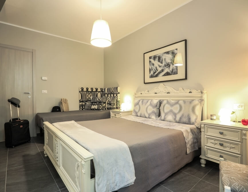 Camera con due letti singoli, comodino bianco, decorazioni moderne e una valigia nera vicino alla porta.