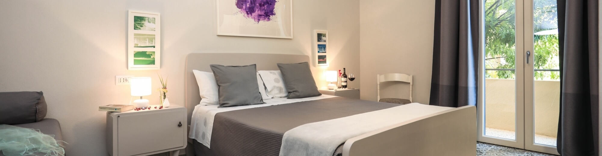 Camera da letto serena con letto taupe, finestre grandi, quadri sopra il letto e un'atmosfera rilassante.