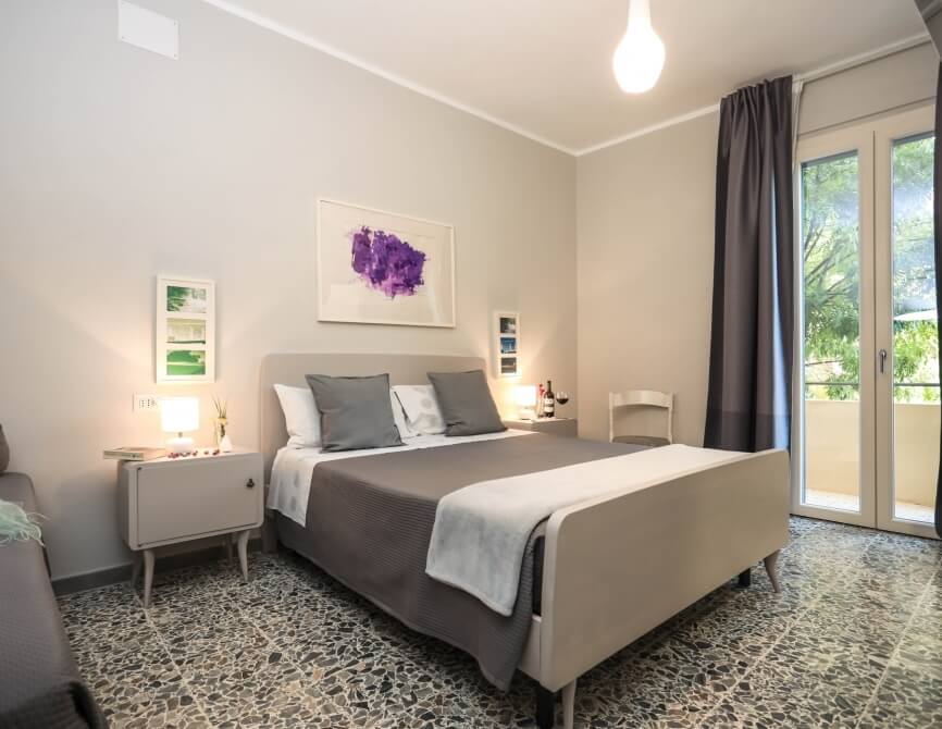 Camera d'hotel con letto, comodini, sedia e balcone.