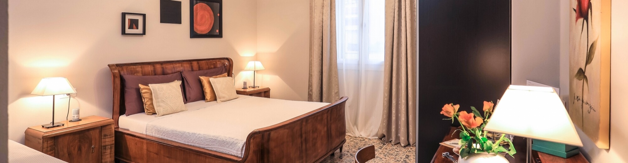 Camera serena con letto in legno scuro, biancheria bianca, opere d'arte, finestre luminose e fiori freschi.