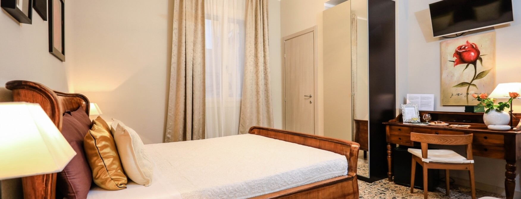 Camera accogliente con letto, scrivania, lampada, armadio e televisore, decorata con fiori e un dipinto di rosa rossa.