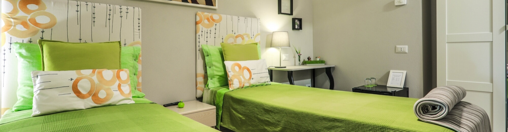 Due letti gemelli con biancheria verde e bianca, testiere floreali, comodini e lampade in una camera d'hotel accogliente.