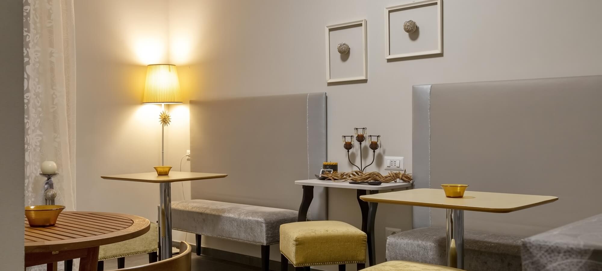 Area pranzo accogliente con tavoli, sedie, ciotole gialle e decorazioni, illuminata da una lampada tra i tavoli.