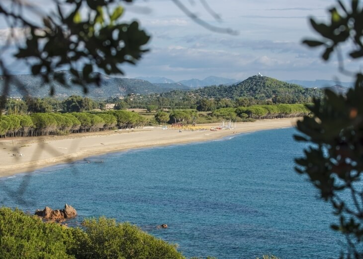 Vista costiera con spiaggia sabbiosa, acqua blu e colline verdi.