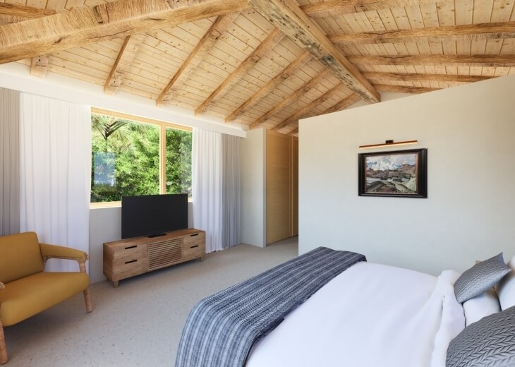 Camera d'hotel con letto, poltrona gialla e vista sugli alberi.