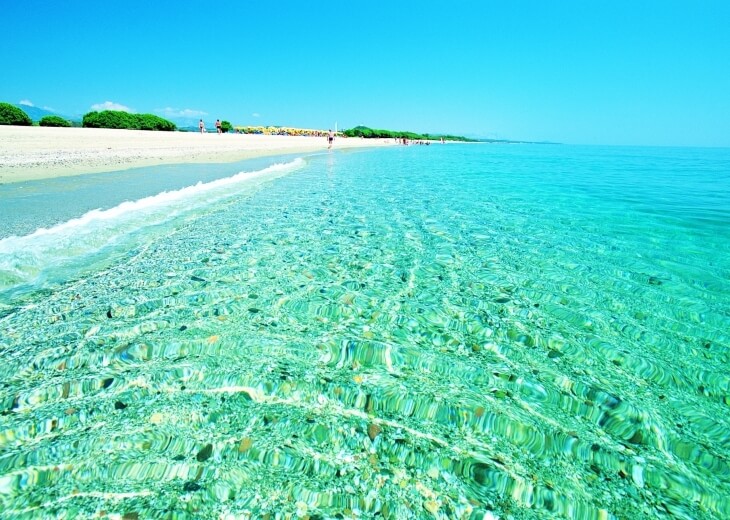 Spiaggia tranquilla con cielo blu, acqua turchese e onde bianche.