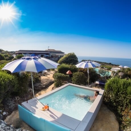 Persona rilassata in jacuzzi con ombrelloni, vista sull'oceano.